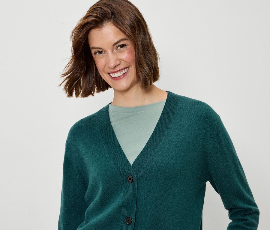 Lächelnde Frau mit kurzem braunem Haar trägt eine grüne Strickjacke und ein grünes T-Shirt.
