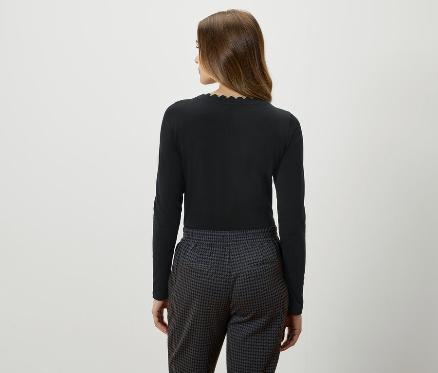 Rückansicht einer Frau mit braunen Haaren in einem schwarzen Langarmshirt und grau-schwarzen Hosen.