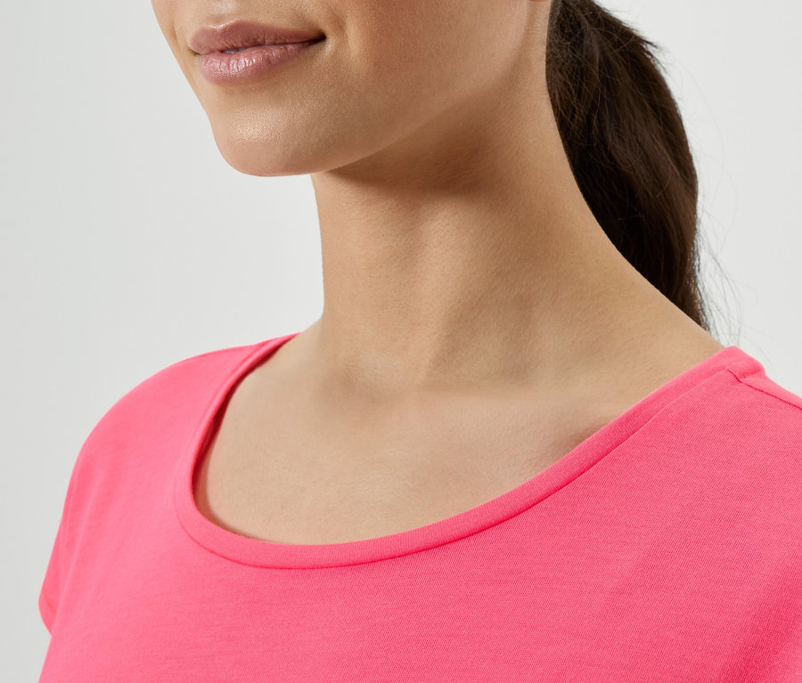 Oberkörper einer Frau mit dunklen Haaren, die zu einem Pferdeschwanz gebunden sind, trägt ein pinkes T-Shirt.