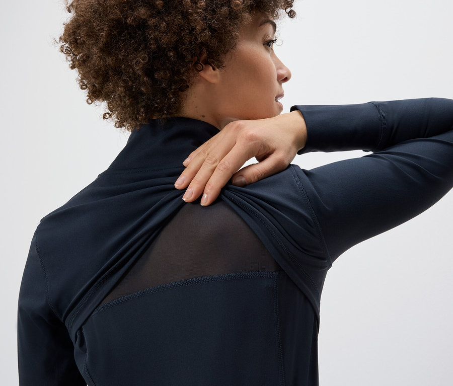 Frau zieht Funktionsjacke über ihre Schulter, wodurch ein Netzstoffeinsatz am Rücken sichtbar wird.
