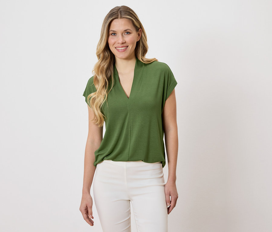 Frau trägt eine grüne Bluse und weiße Hose.
