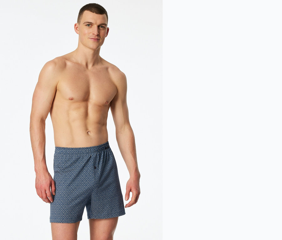 Mann mit freiem Oberkörper und blauen Boxershorts mit geometrischem Muster.