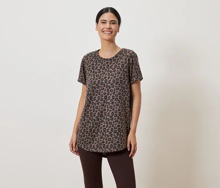 Eine Frau mit hochgesteckten Haaren trägt ein braunes Leopardenmuster-T-Shirt und braune Leggings vor einem hellen Hintergrund.