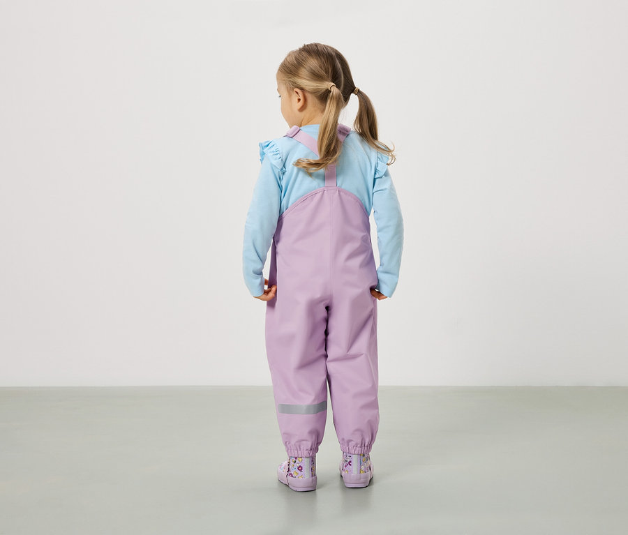 Ein Mädchen mit Zöpfen steht mit dem Rücken zur Kamera und trägt eine lila Hose und passende Stiefel.