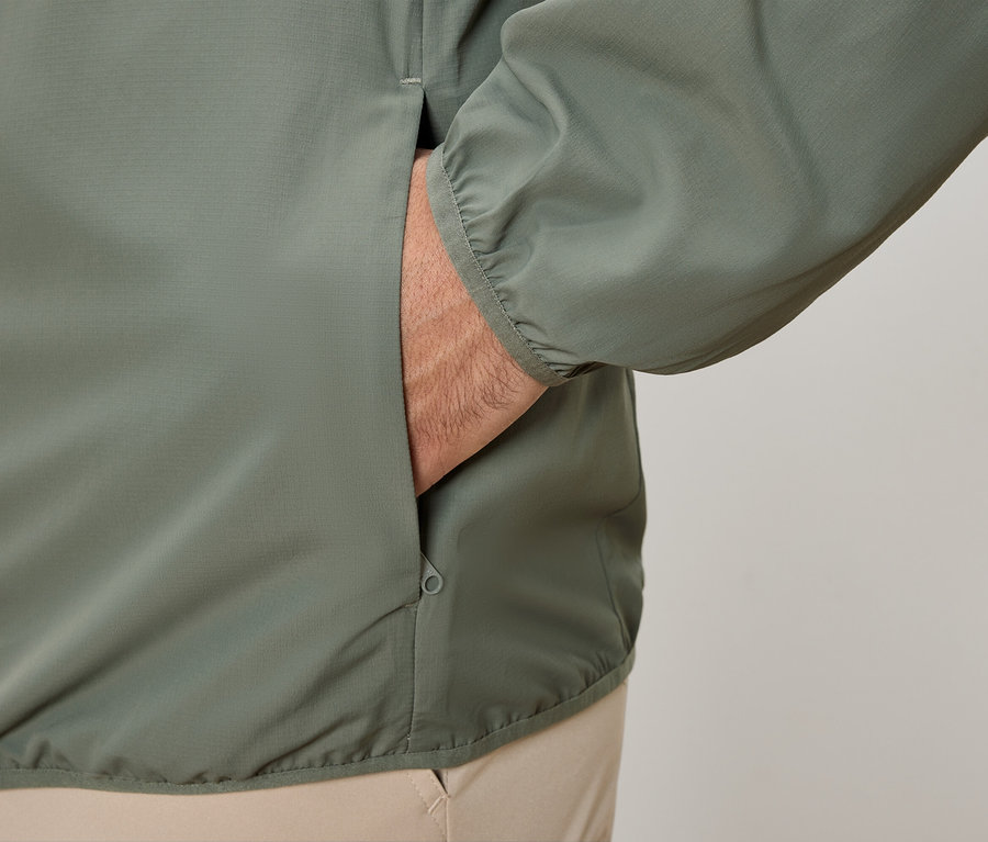 Nahaufnahme einer Person, die ihre Hand in die Tasche einer olivgrünen Jacke steckt.