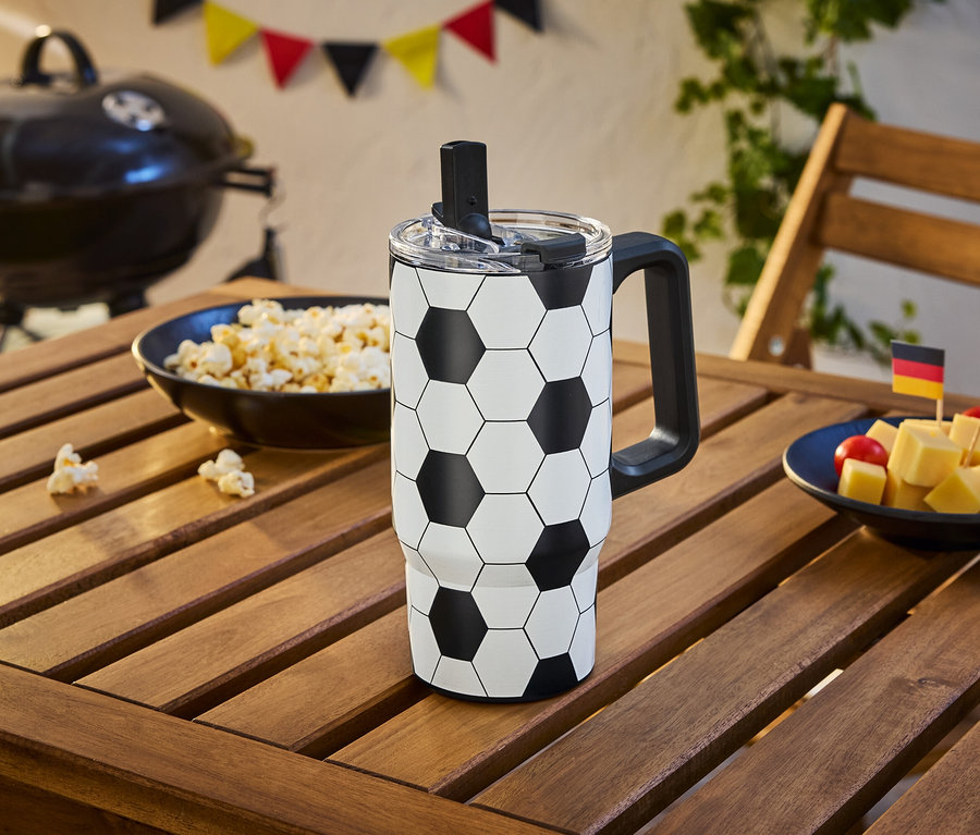 Ein Fußballbecher steht auf einem Holztisch neben einer Schüssel Popcorn und Käsewürfeln mit Deutschland- und Spanienflaggen.