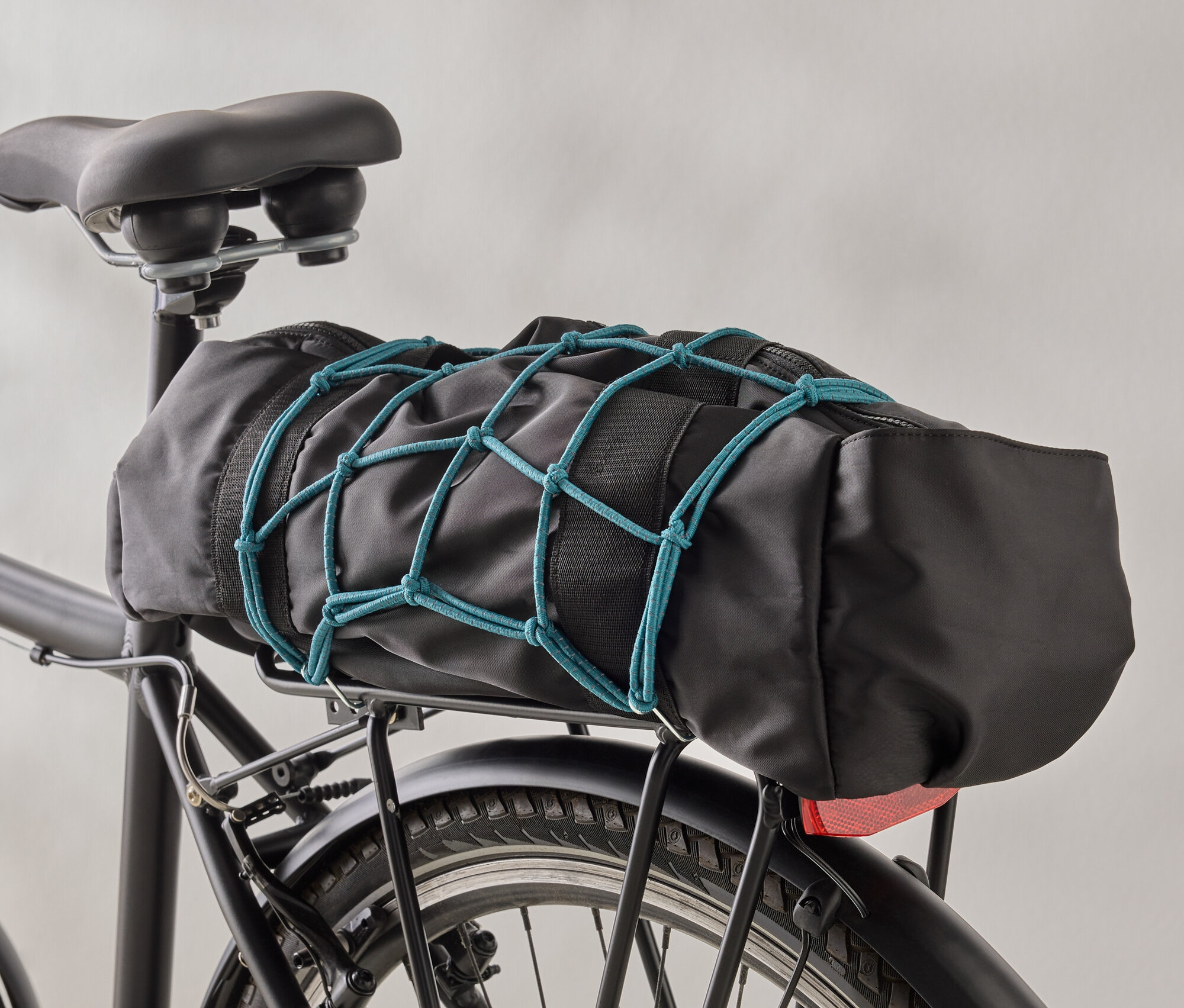 Eine schwarze Fahrradtasche ist mit einem blauen Gepäcknetz auf einem schwarzen Fahrradgepäckträger befestigt.