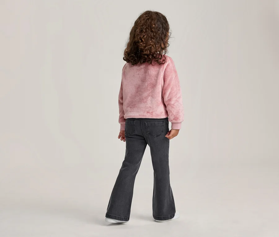 Mädchen von hinten mit lockigem Haar, rosa flauschigem Pullover und dunkelgrauen Schlagjeans.