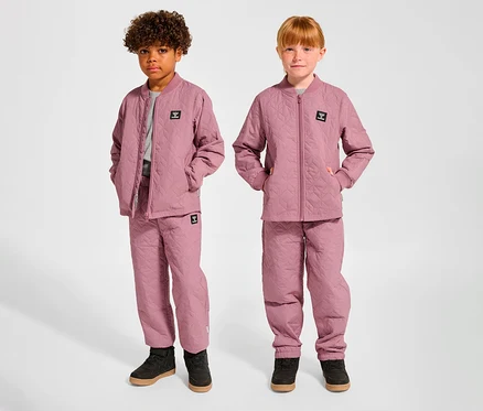 Zwei Kinder, ein Junge und ein Mädchen, stehen nebeneinander und tragen passende rosa hummel® HMLSOBI Thermo-Sets, bestehend aus gesteppten Jacken und Hosen.