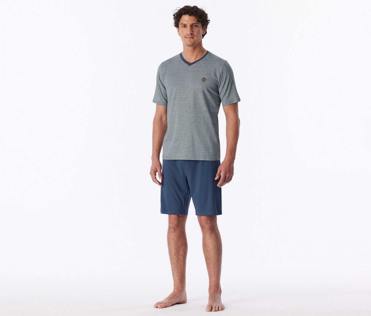 Mann steht barfuß und trägt ein graues V-Ausschnitt-T-Shirt und blaue Shorts.