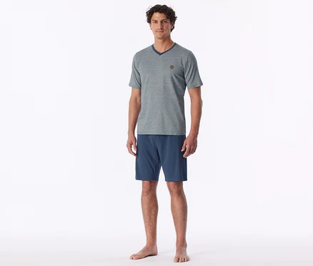 Mann steht barfuß und trägt ein graues V-Ausschnitt-T-Shirt und blaue Shorts.