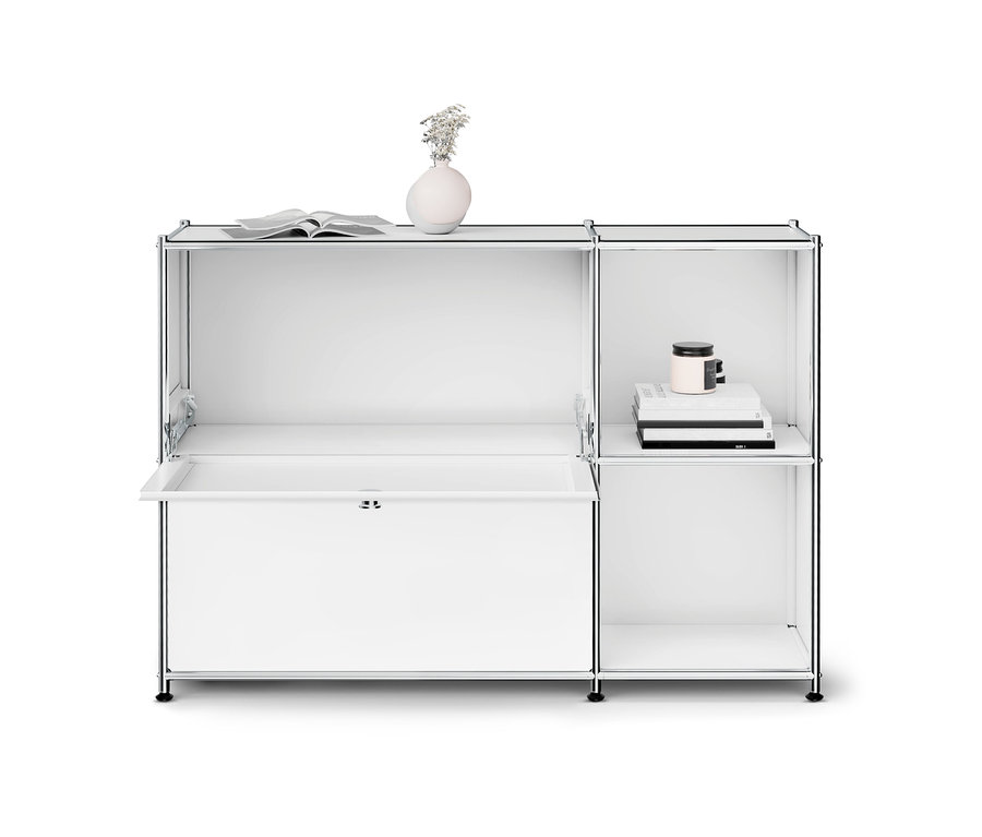Weißes modulares Regal mit Chromrahmen, links eine teilweise geöffnete Klapptür, oben ein offenes Buch und eine Vase mit Blumen, rechts oben Bücher und eine Kerze.