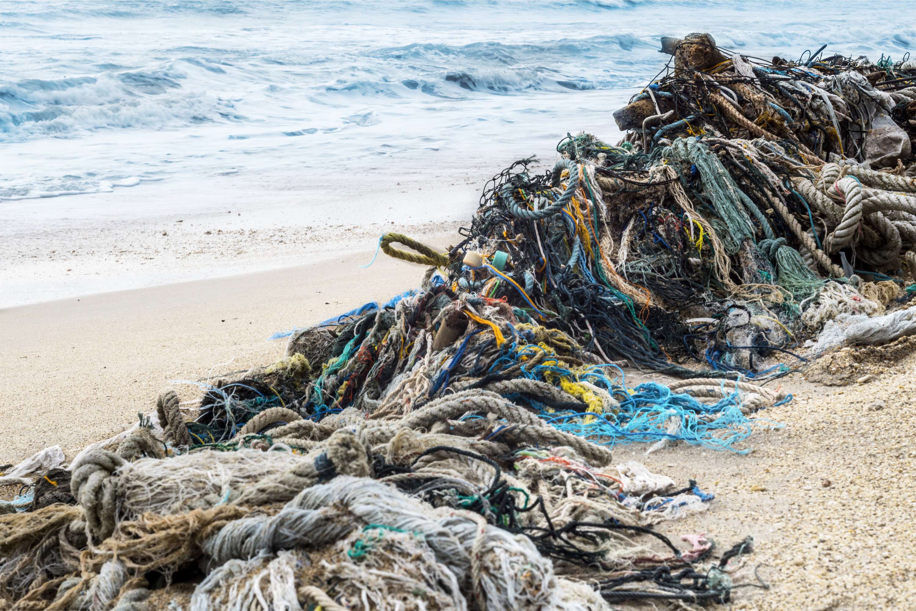 Ein Haufen bunter Seile und Netze liegt am Strand nahe den Wellen.