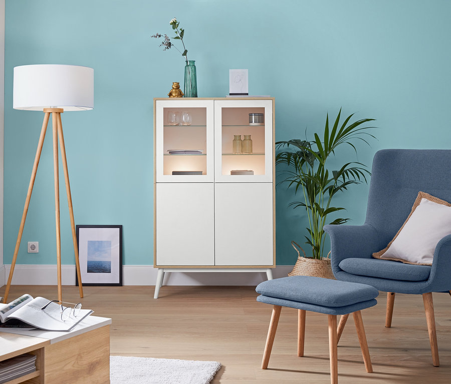 Wohnzimmer mit »Dreibein«-Stehleuchte aus Holz, Sessel mit Fußhocker und LED-Lichtleiste.