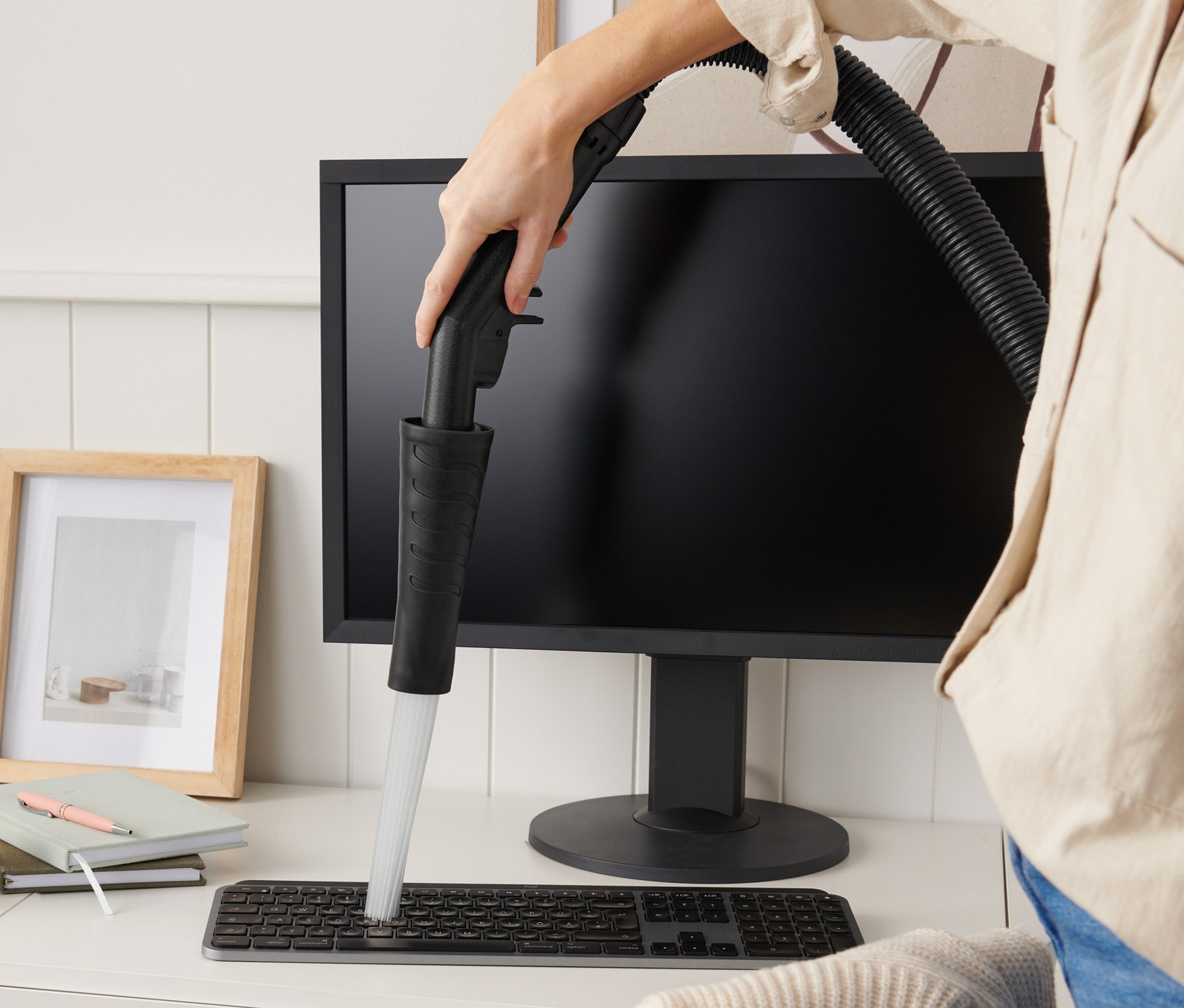 Frau reinigt eine Tastatur mit einem Staubsaugeraufsatz auf einem Schreibtisch.