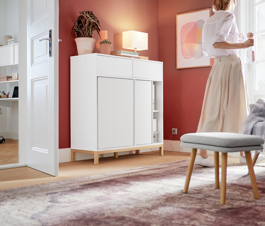 Frau steht im Zimmer neben einem weißen Büroschrank mit Schiebetüren.