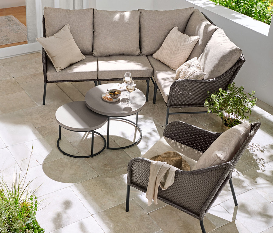 Loungeecke mit Polyrattangeflecht, Loungesessel mit Polyrattangeflecht und 2 Couchtische mit Beton-Tischplatte auf einer Terrasse.