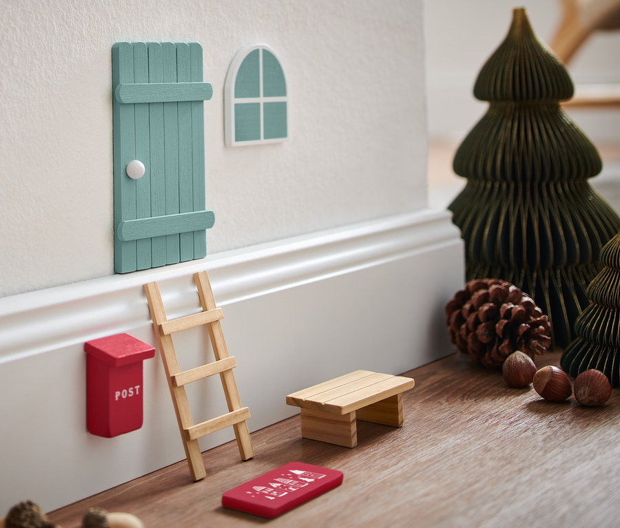Ein Wichteltür-Set an einer Wand mit Miniatur-Weihnachtsbäumen und Deko.