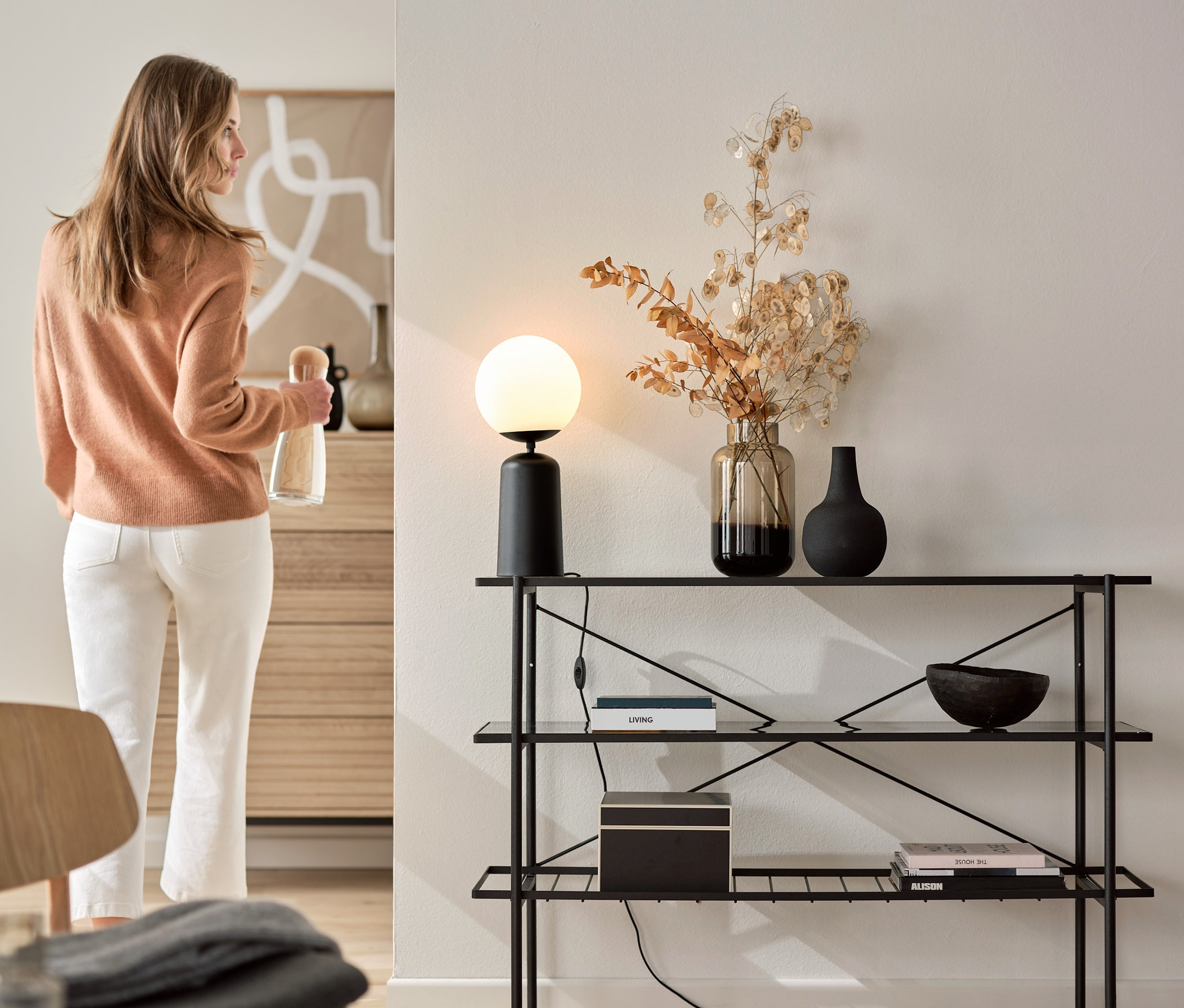 Frau hält Flasche neben Konsole (Breite ca. 120 cm) mit schwarzer Tischleuchte mit Glaskugel.