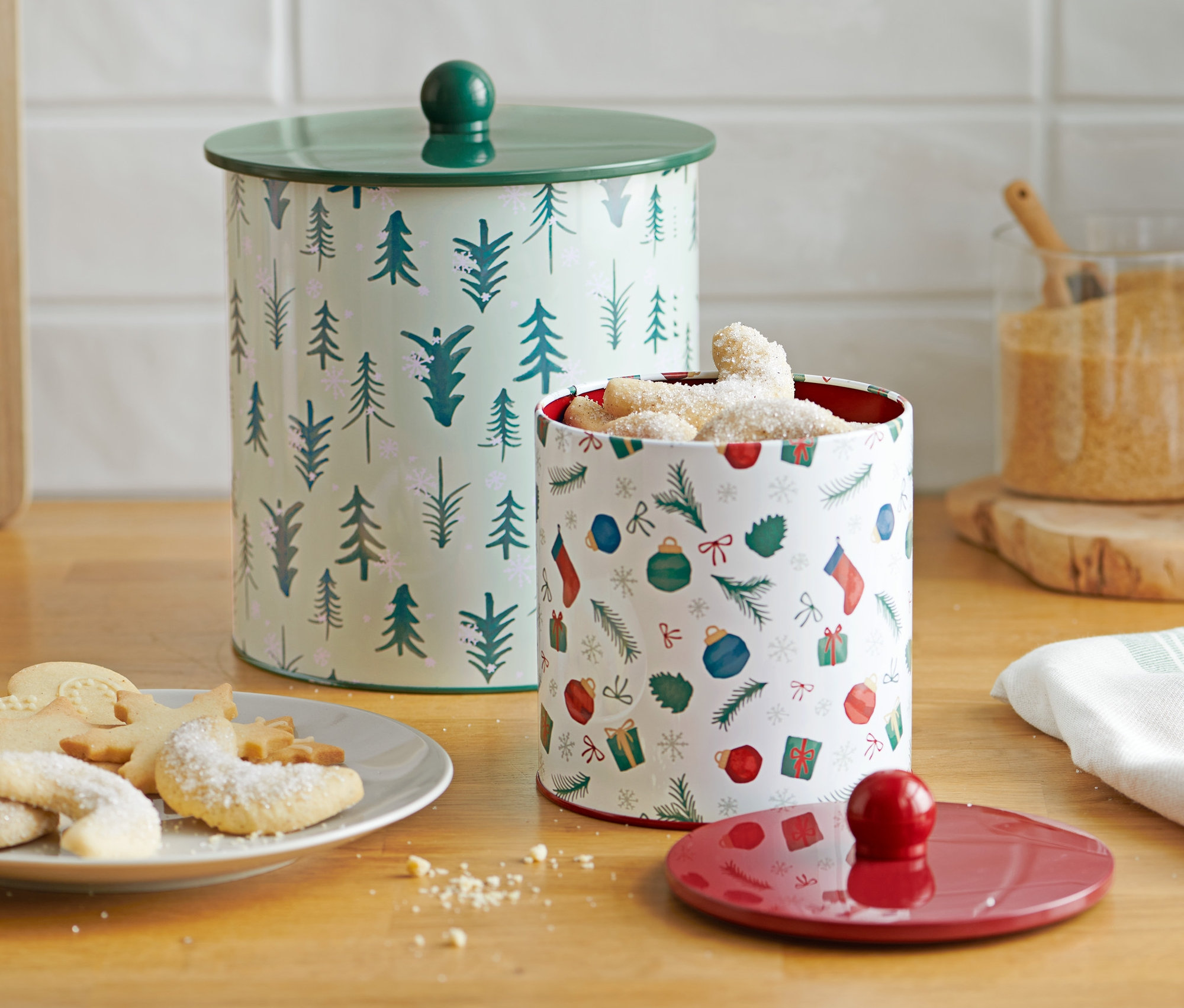 Zwei Keksdosen stehen auf einem Tisch neben einem Teller mit Keksen.
