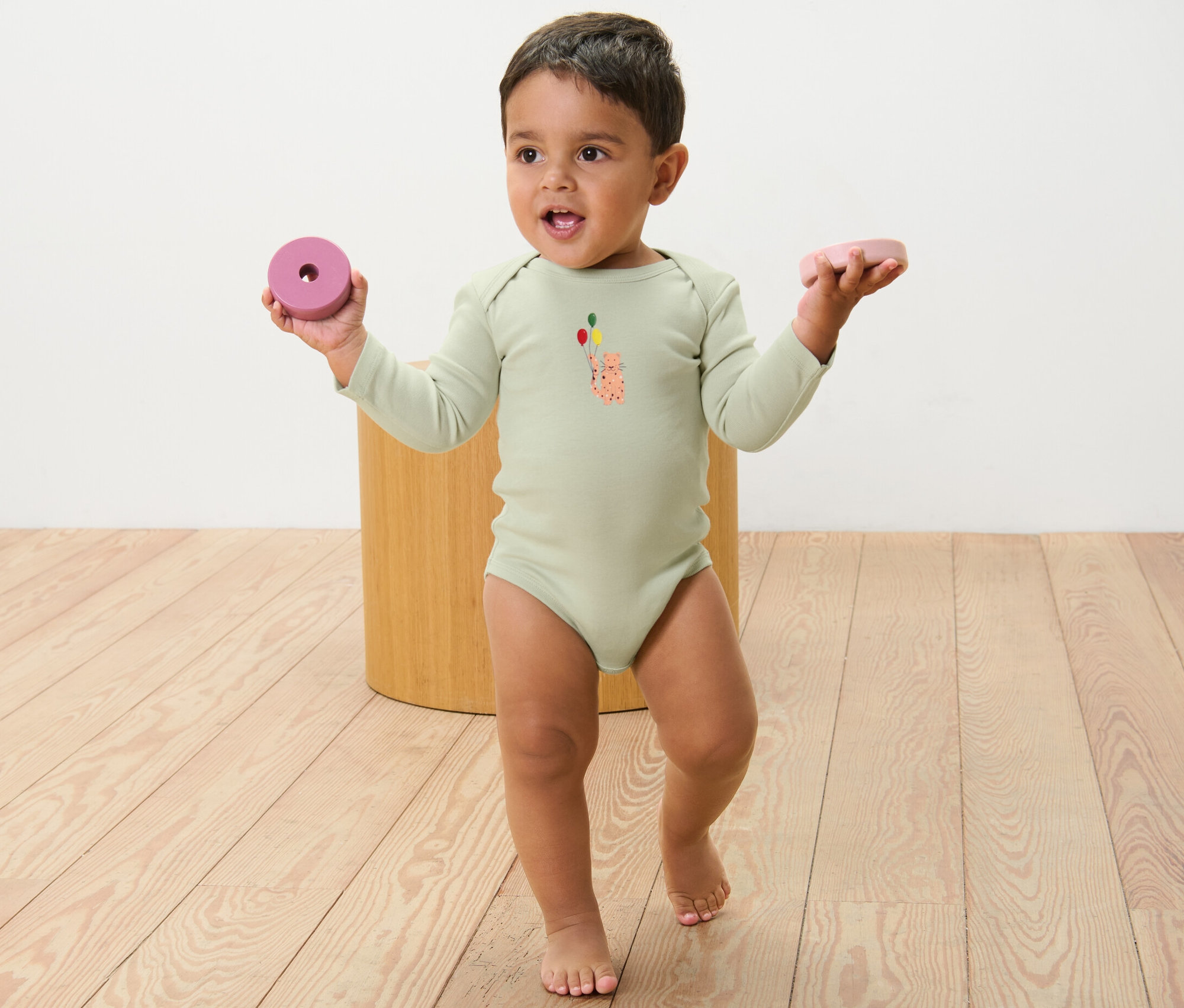 Kleinkind in einem langärmeligen Body mit Aufdruck, das in jeder Hand ein Spielzeug hält. 5 Baby-Bodys mit Mitwachsfunktion