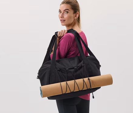 Frau trägt schwarze Sporttasche und Yogamatte über der Schulter.