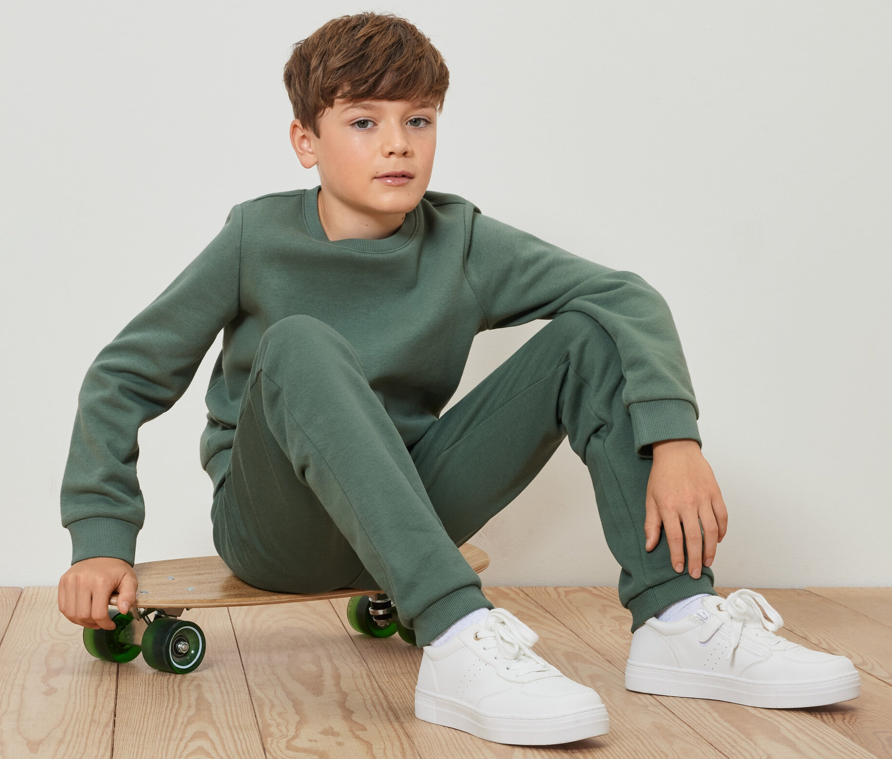 Ein Junge sitzt auf einem Skateboard und trägt eine grüne Kinder-Sweathose.