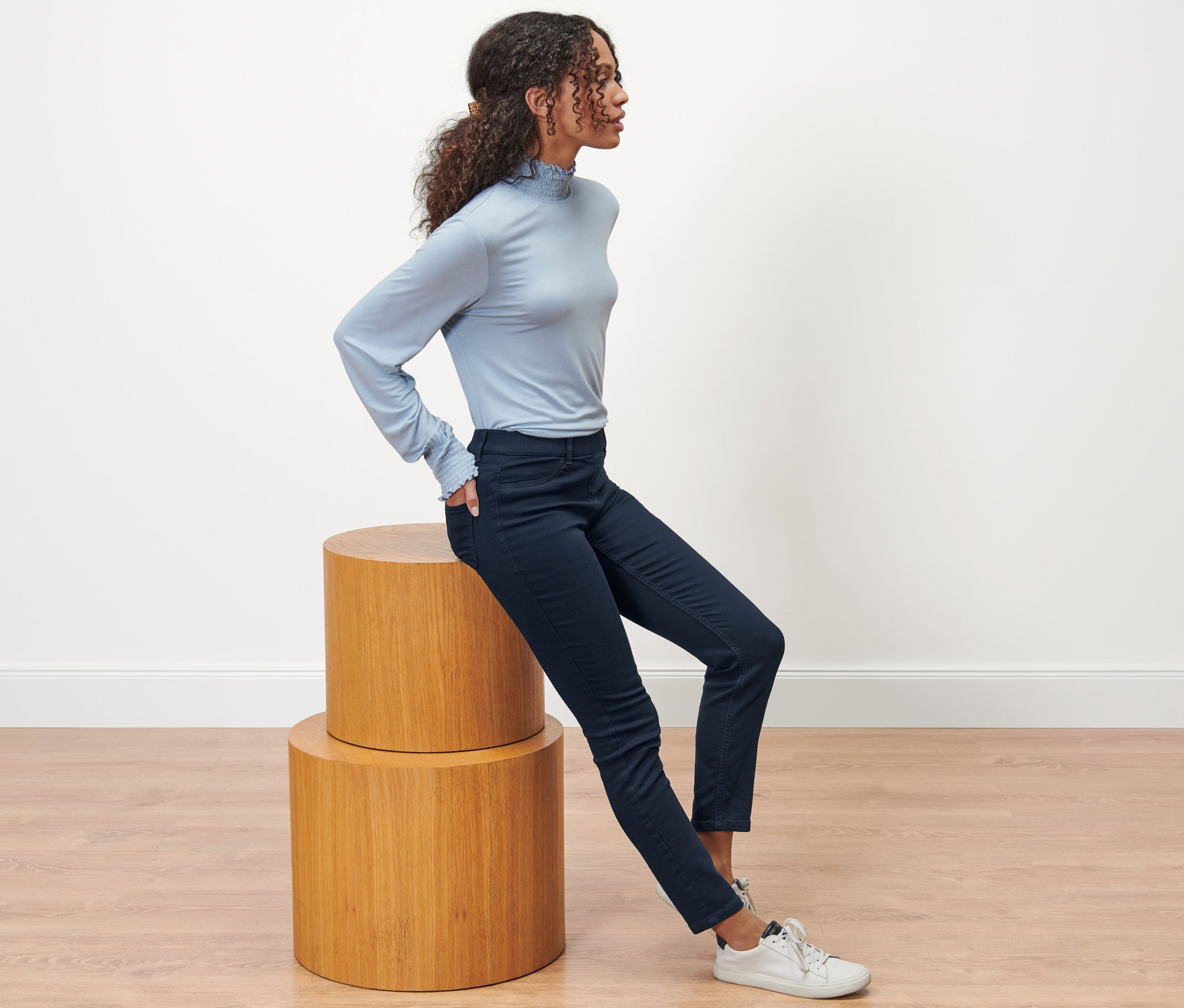 Frau sitzt auf einem Holzhocker und trägt dunkelblaue Treggings – Fit »Nelly«.