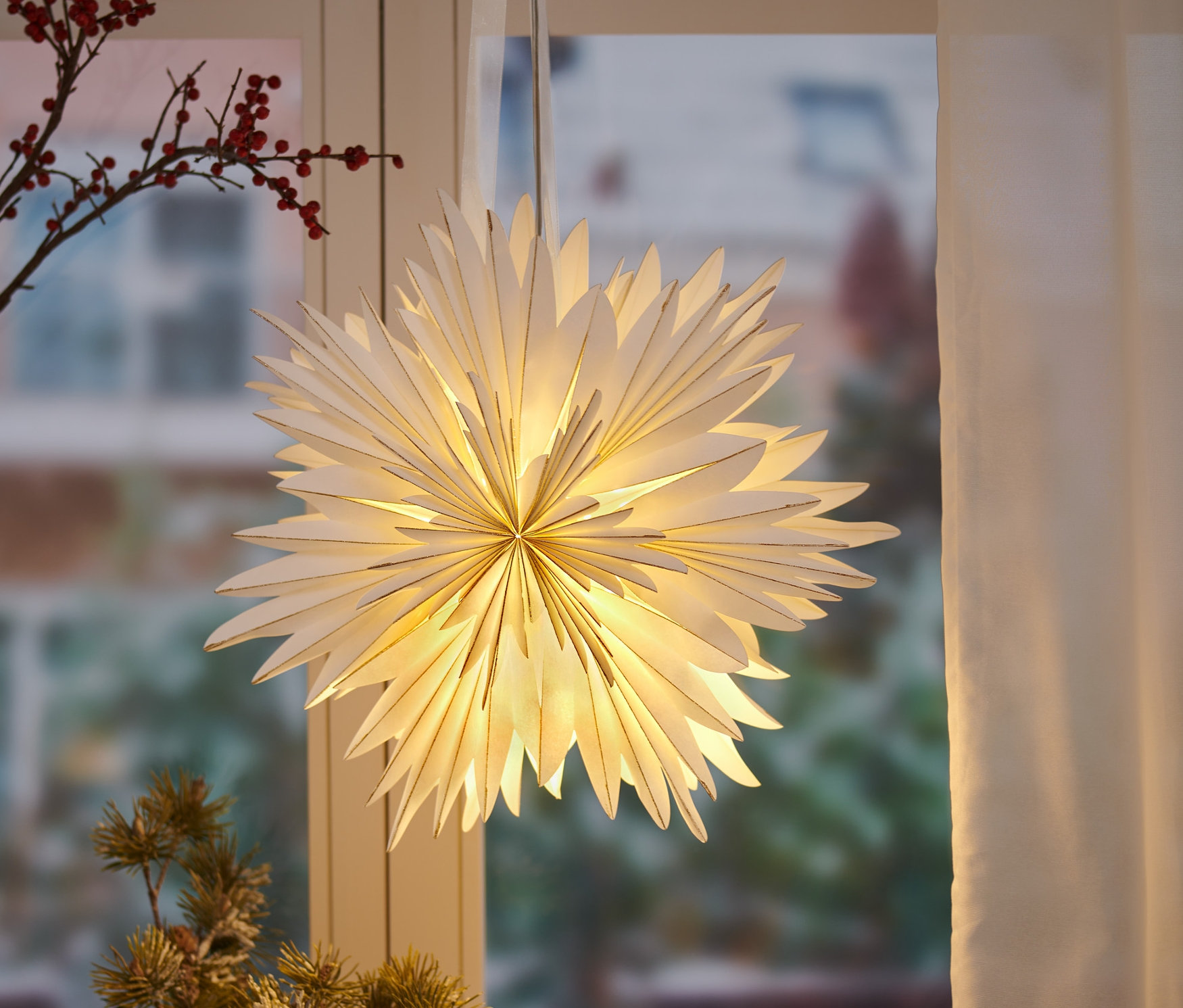 Ein LED-Papierstern hängt vor einem Fenster.