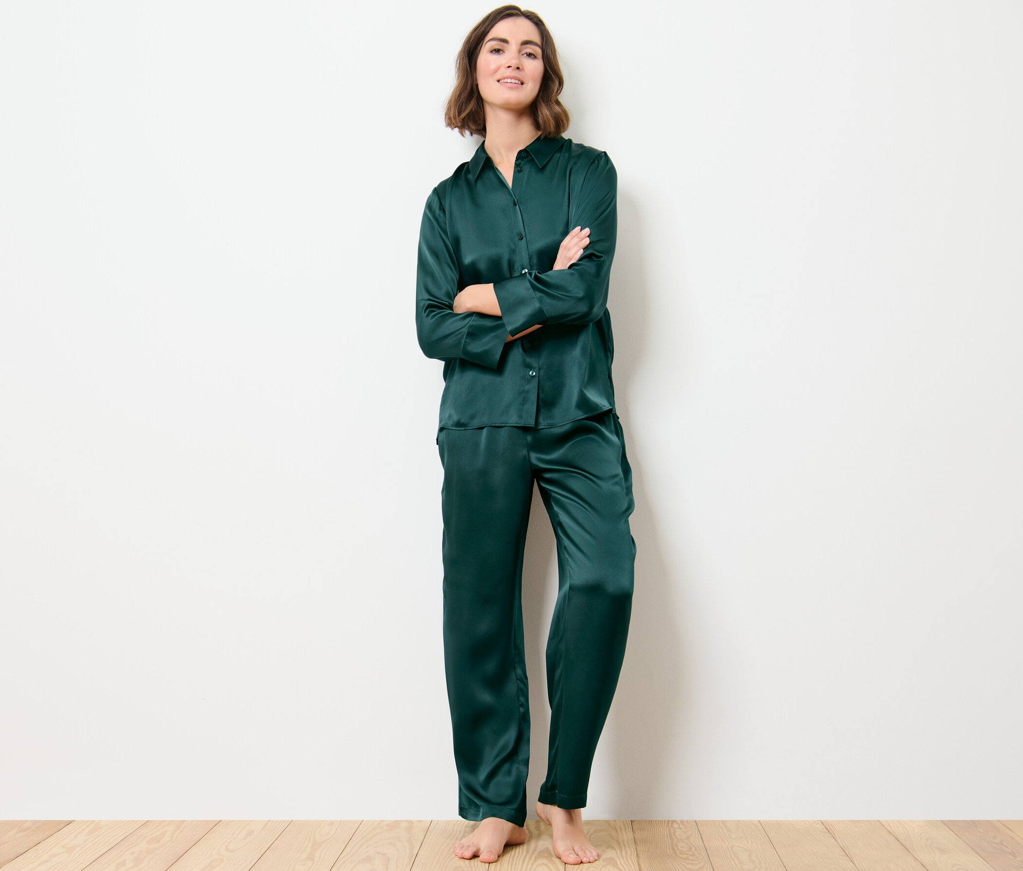 Frau steht mit verschränkten Armen und trägt einen dunkelgrünen Seidenpyjama. Ihr Pyjama-Oberteil aus reiner Seide ist zugeknöpft.