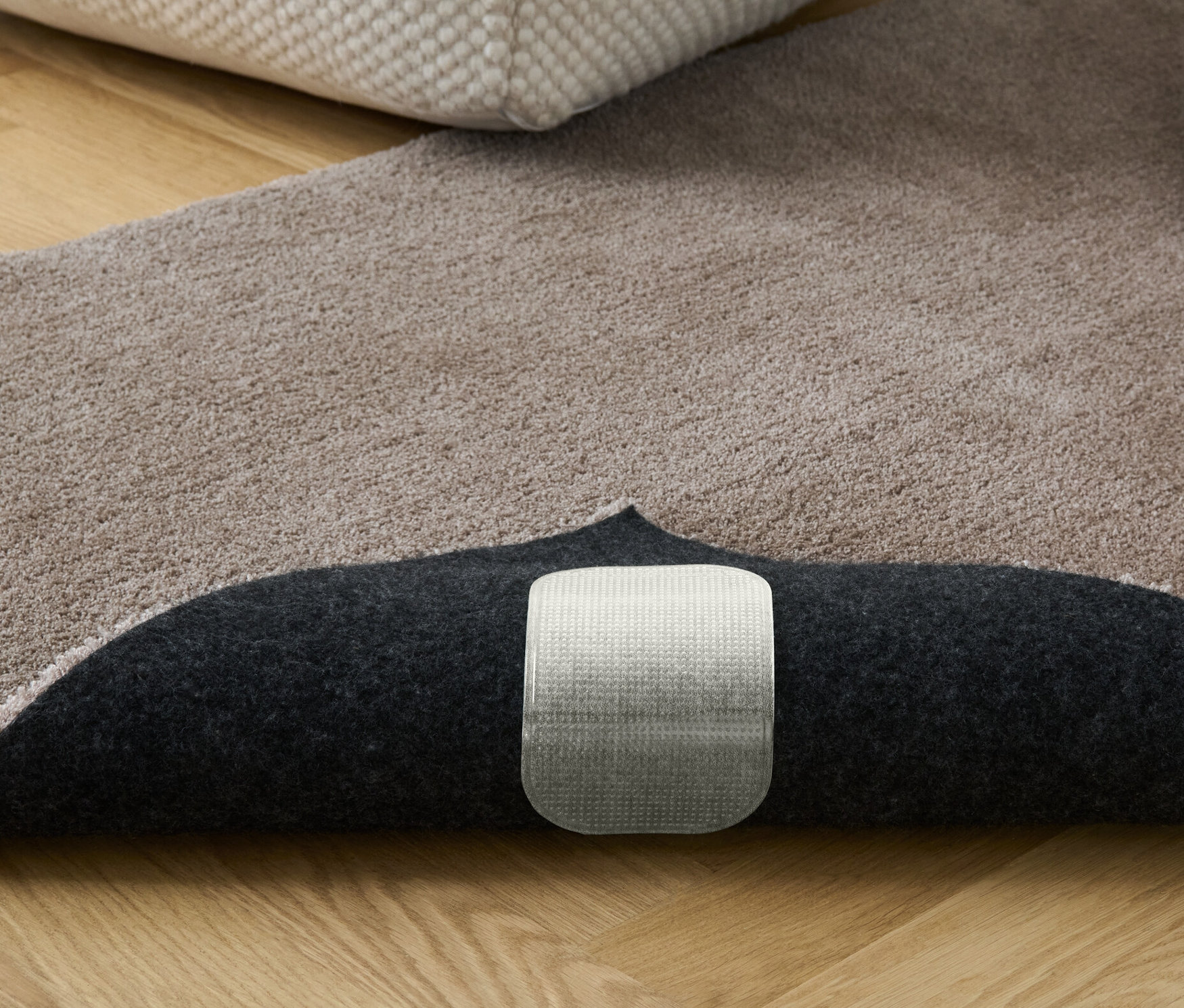 Ein beiger Teppich mit Büchern und einem Hocker. Sichtbar sind 4 Teppich-Antirutsch-Unterlagen.