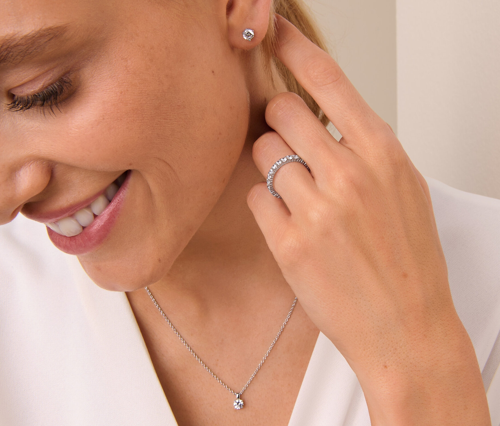 Frau lächelt und berührt ihr Ohr, sie trägt einen 925 Silber Ring Memory, eine 925 Silber Kette Solitär und 925 Silber Ohrstecker Solitär.