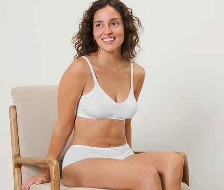 Frau sitzt auf einem Stuhl und trägt einen weißen Seamless-Soft-BH.