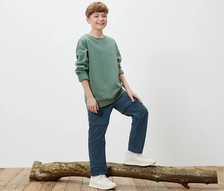 Ein Junge steht auf einem Baumstamm und trägt eine Kinder-Funktionshose.