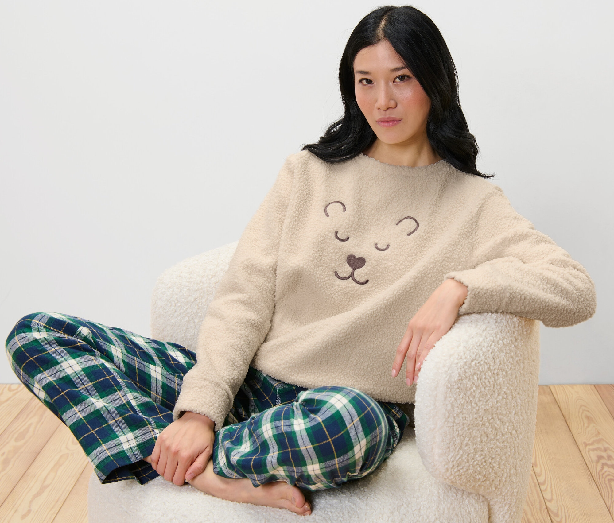 Frau sitzt im Sessel und trägt einen Kuschel-Sweater und eine karierte Hose.