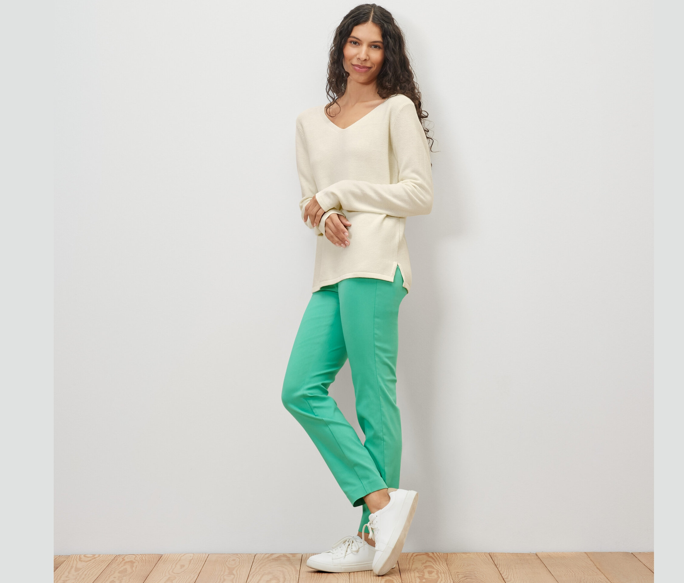 Frau posiert vor hellem Hintergrund und trägt einen cremeweißen Strickpullover.