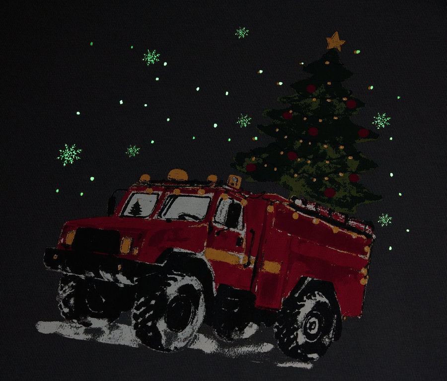 Ein rotes Feuerwehrauto transportiert einen Weihnachtsbaum im Schneefall.