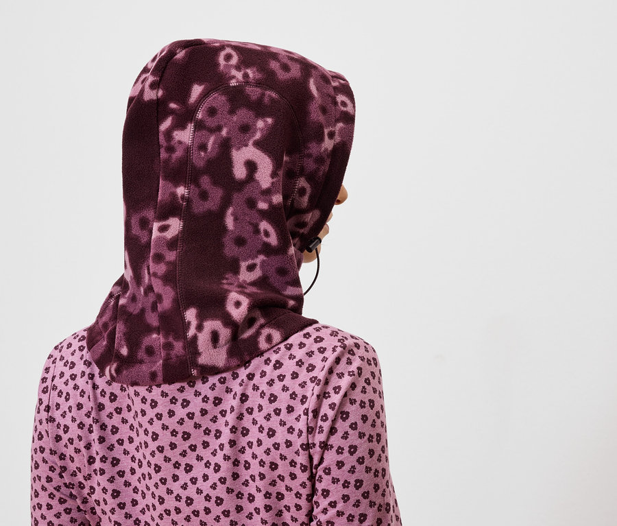 Rückansicht einer Frau mit einem lila geblümten Hidschab und einem lila Hemd mit Herzmuster.