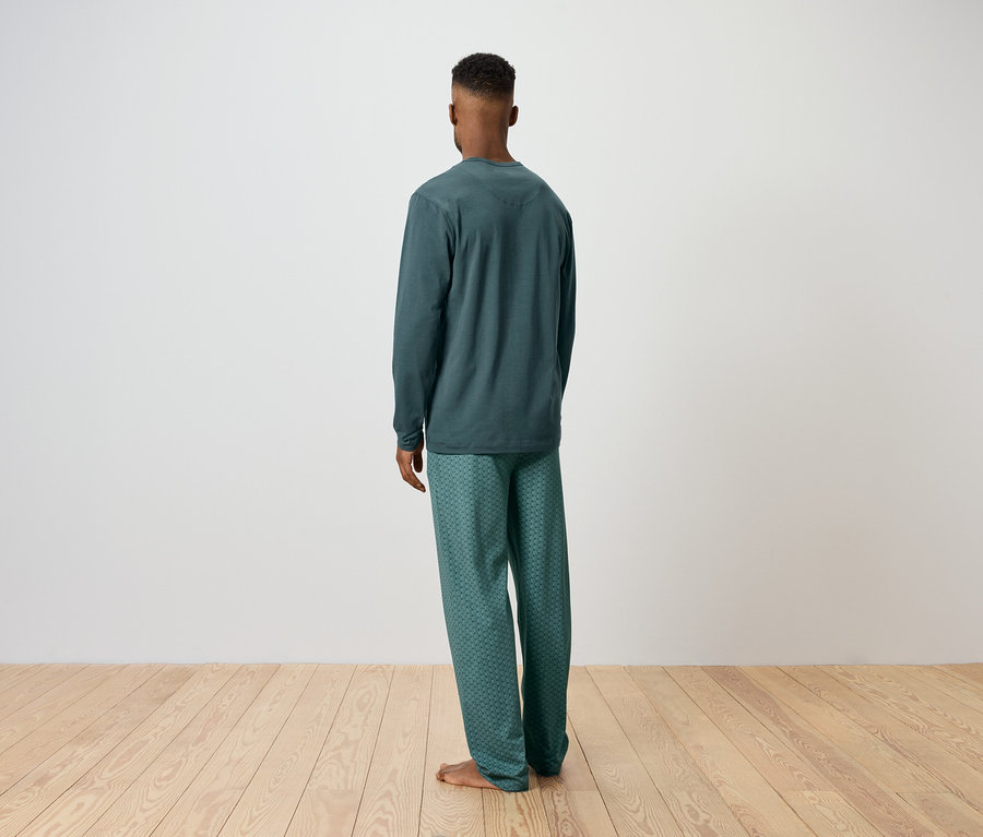 Mann steht mit dem Rücken zur Kamera und trägt einen grünen Pyjama.