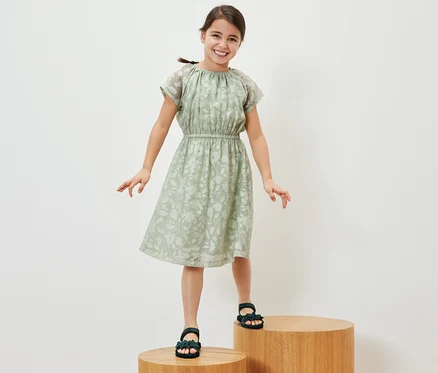 Ein lächelndes Mädchen steht auf Holzstufen und trägt ein Kinder-Kleid.
