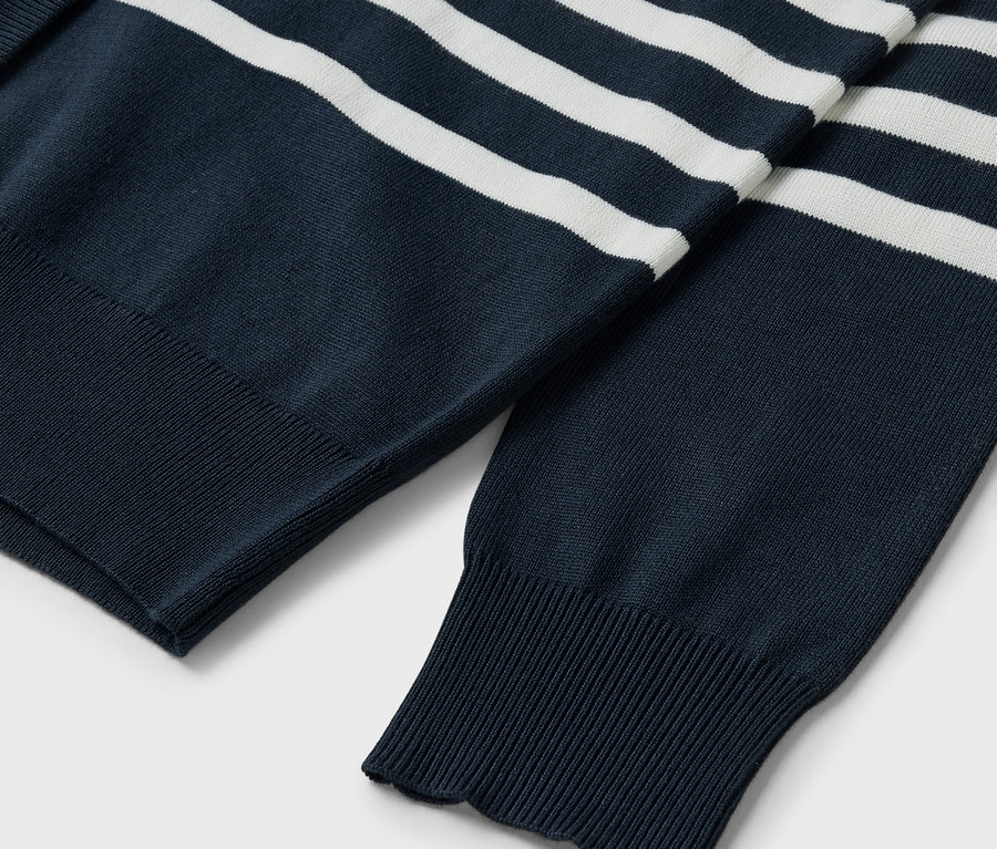 Detailansicht eines dunkelblauen Pullovers mit weißen Streifen, Ärmel und gerippte Bündchen sichtbar.