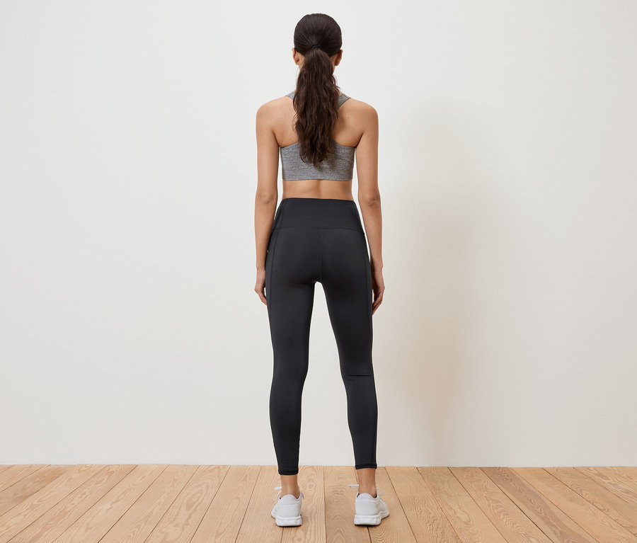 Frau mit grauem Sport-BH und schwarzen Leggings steht mit dem Rücken zur Kamera.