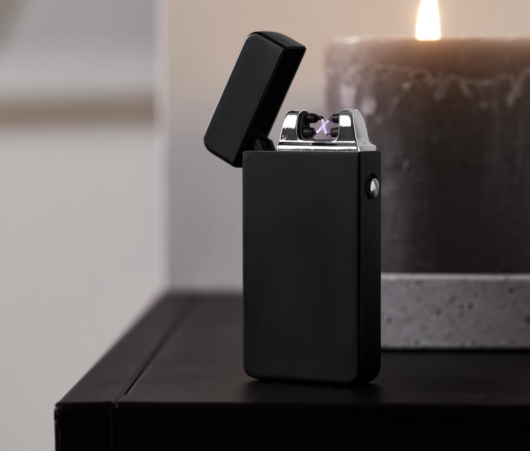 Ein schwarzes elektrisches Feuerzeug steht auf einem Tisch neben einer brennenden Kerze.