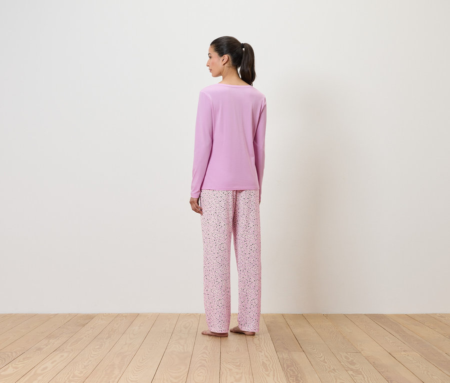 Frau im lila Pyjama mit Blumenmuster, die mit dem Rücken zum Betrachter steht.