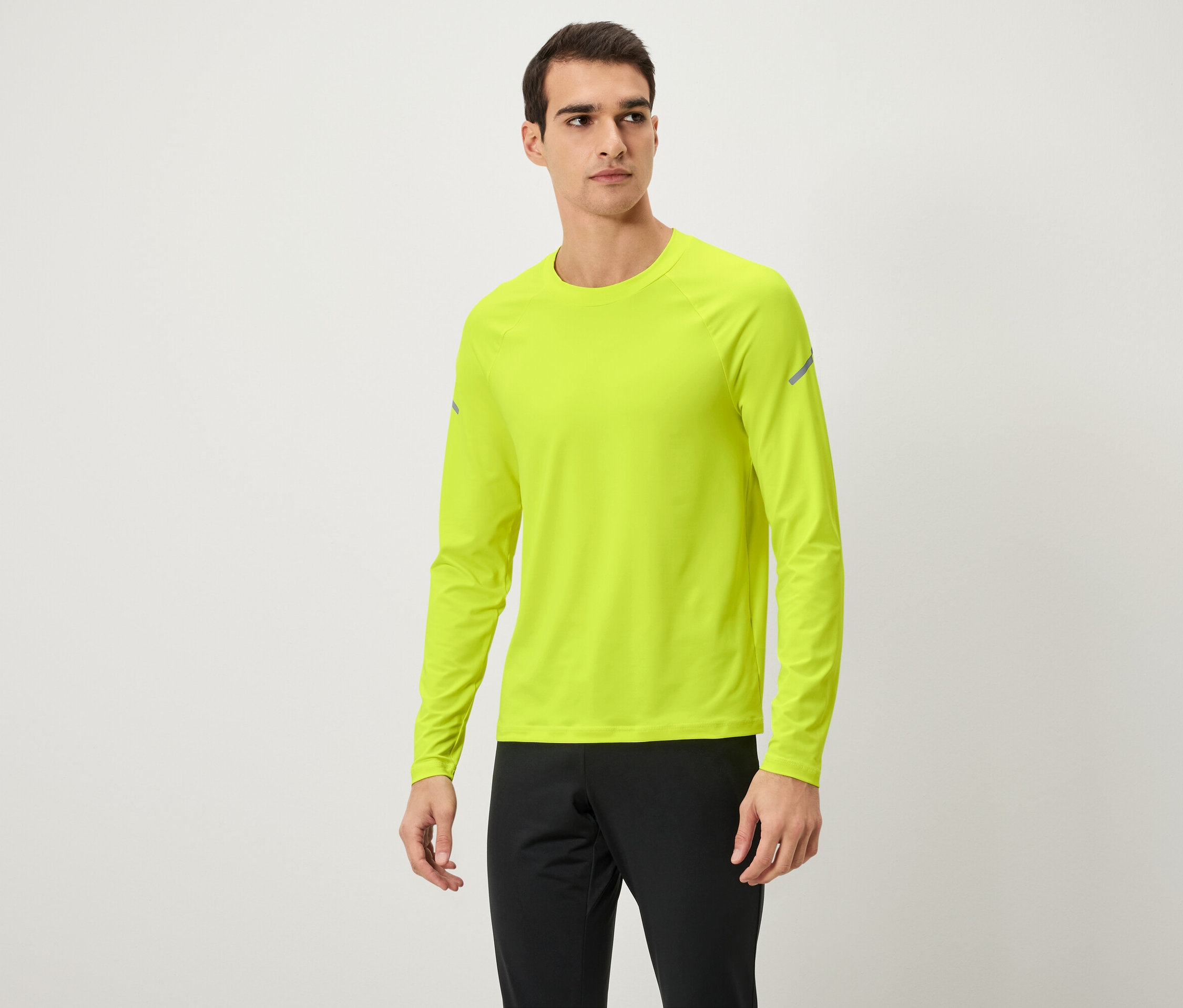 Mann posiert in neongelbem Langarmshirt und schwarzer Trainingshose.