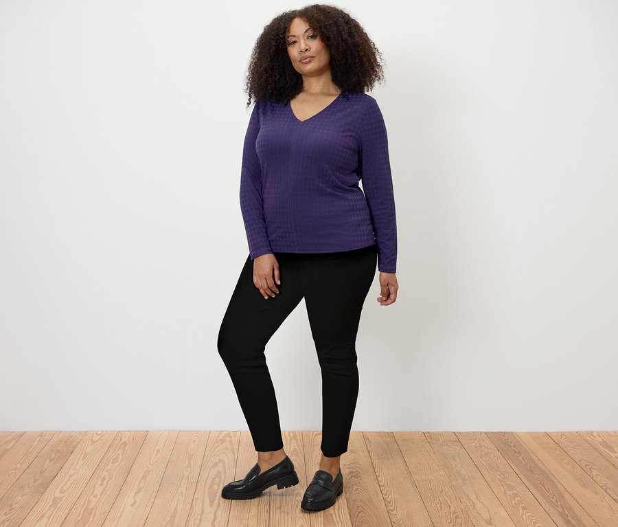 Frau posiert in einem strukturierten Langarmshirt in Pflaume und Jeggings.