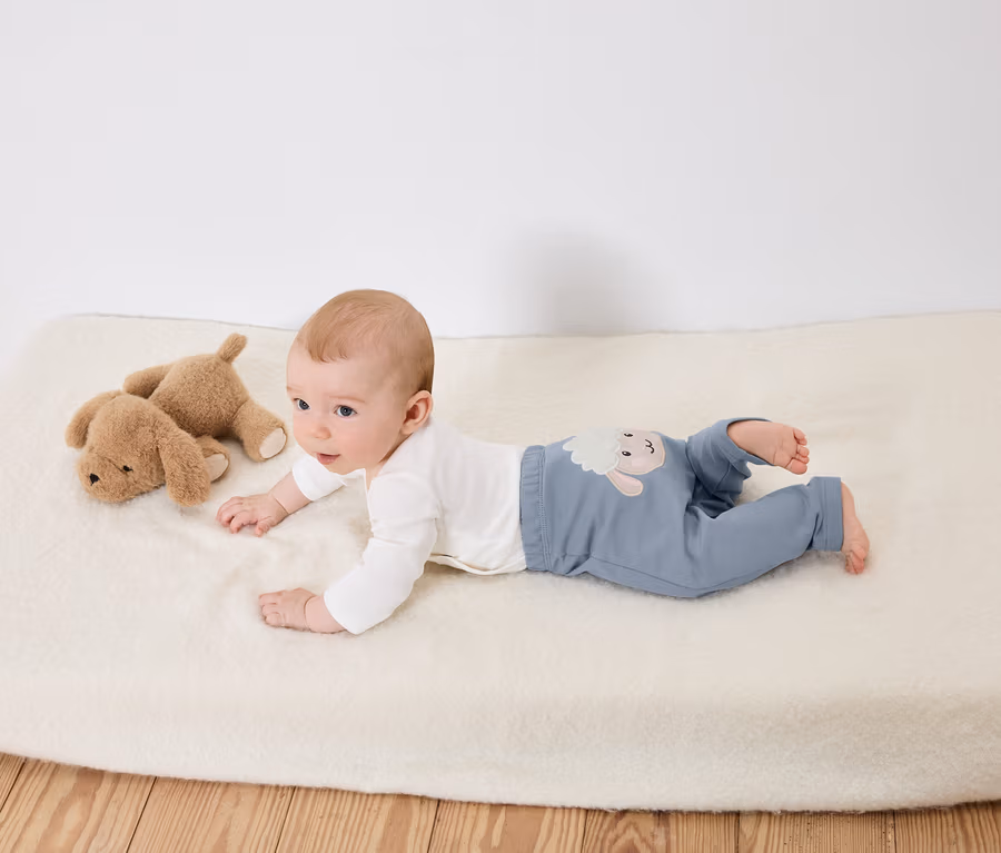 Baby liegt auf dem Bauch auf einer weißen Unterlage neben zwei braunen Stoffhunden.