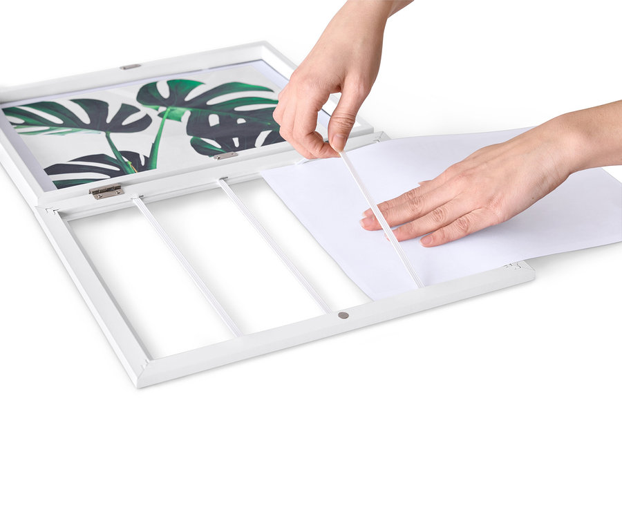 Hände legen ein weißes Blatt Papier in einen aufklappbaren Bilderrahmen.
