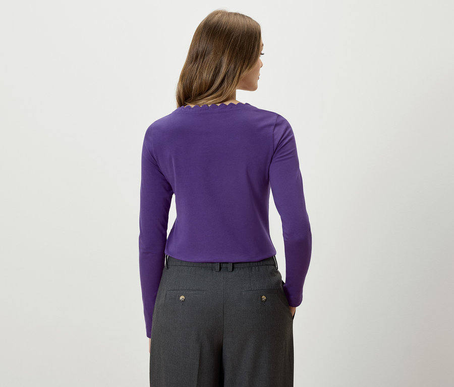 Frau mit dem Rücken zur Kamera trägt ein lila Langarmshirt und eine graue Hose.