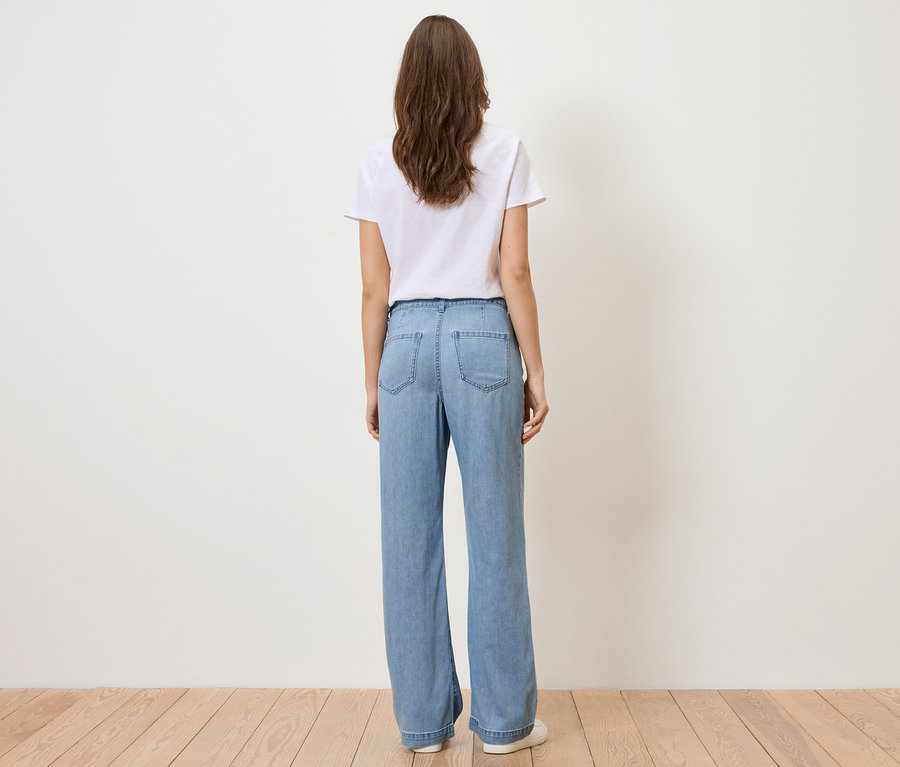 Rückansicht einer Frau mit langen braunen Haaren, die ein weißes T-Shirt und hellblaue Jeans trägt.